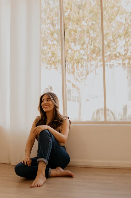 Smiling woman sitting in a lotus pose in a sunlit living room